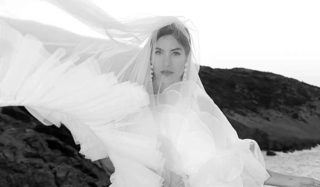 Nevesta u venčanici, veo talasa na vetru uz stenovitu obalu — crno-bela fotografija